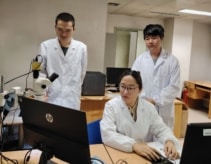 Three memristor project members in the lab, wearing white coats and looking at a computer screen