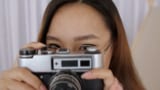 A female photographer wearing glasses, holding a camera