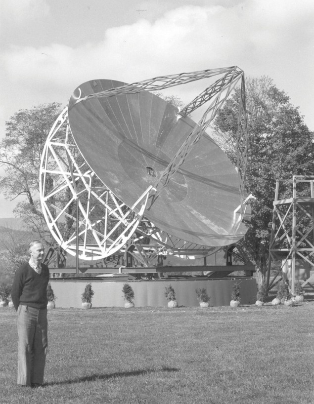 Foto em preto e branco de um homem em frente a um radiotelescópio