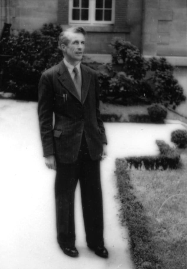 Fotografia em preto e branco de um homem de terno do lado de fora de uma casa grande