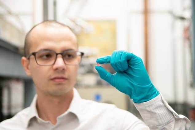 Christopher Simon segura um cristal de fluoreto de lítio, hólmio e ítrio na mão enluvada